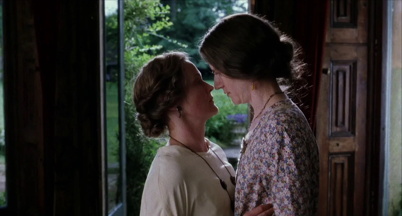 The Hours (2002) movie still: medium — Two women stand face-to-face within the frame of an open wooden door. A green garden is visible through the…