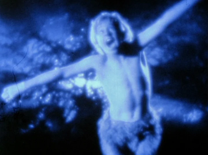 Scorpio Rising (1963) movie still: medium — A dark, indistinct outdoor setting is shrouded in a deep blue nighttime light. A young male figure…