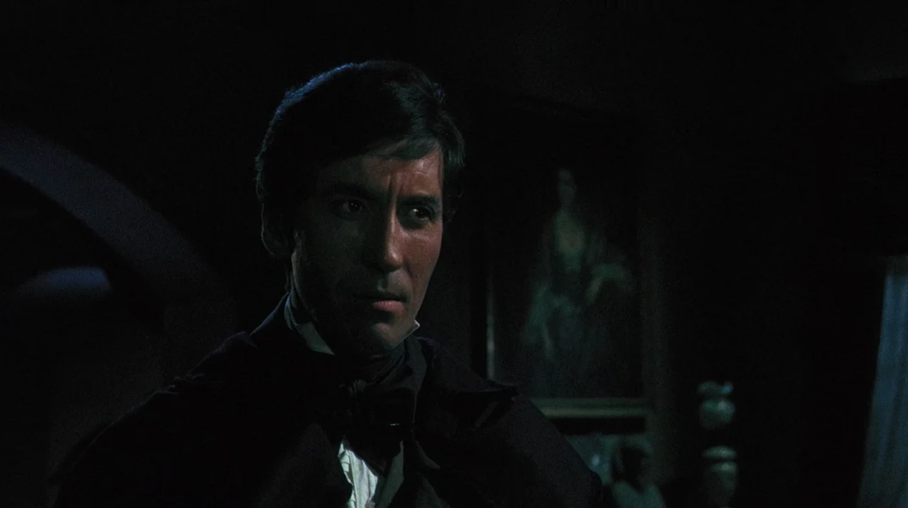 The Whip and The Body (1963) movie still: closeup — A dimly lit, shadow-filled room features a single portrait visible on the wall behind. The man…