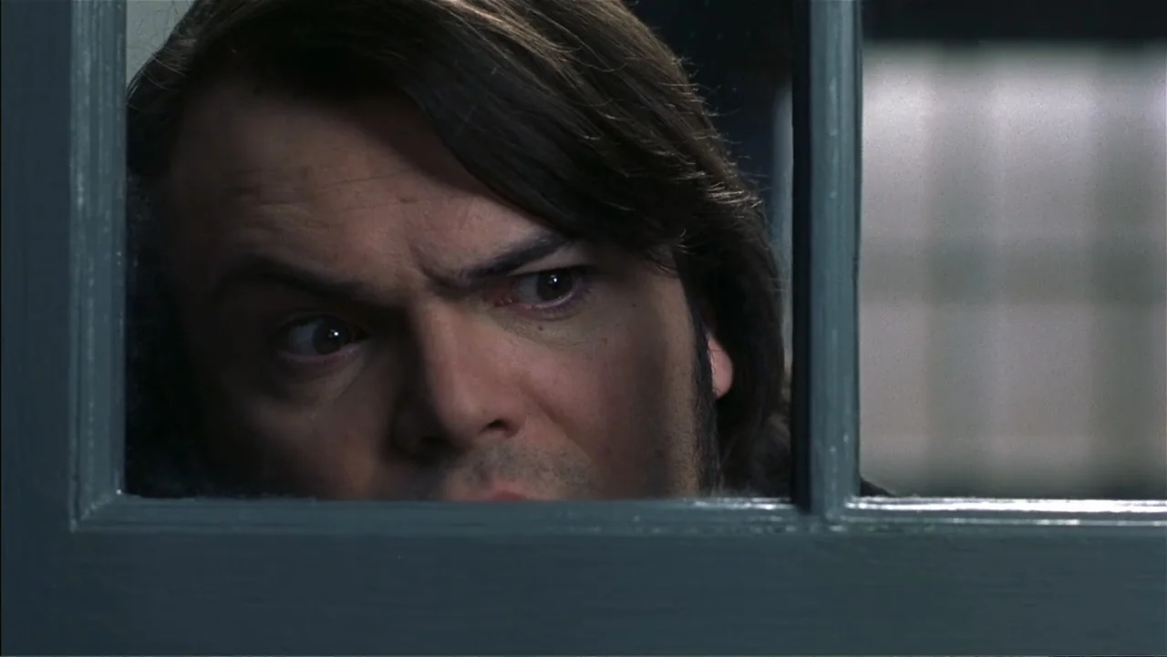 School of Rock (2003) movie still: closeup — A close view through a wooden window frame shows a man looking inward. The subject presses his face…