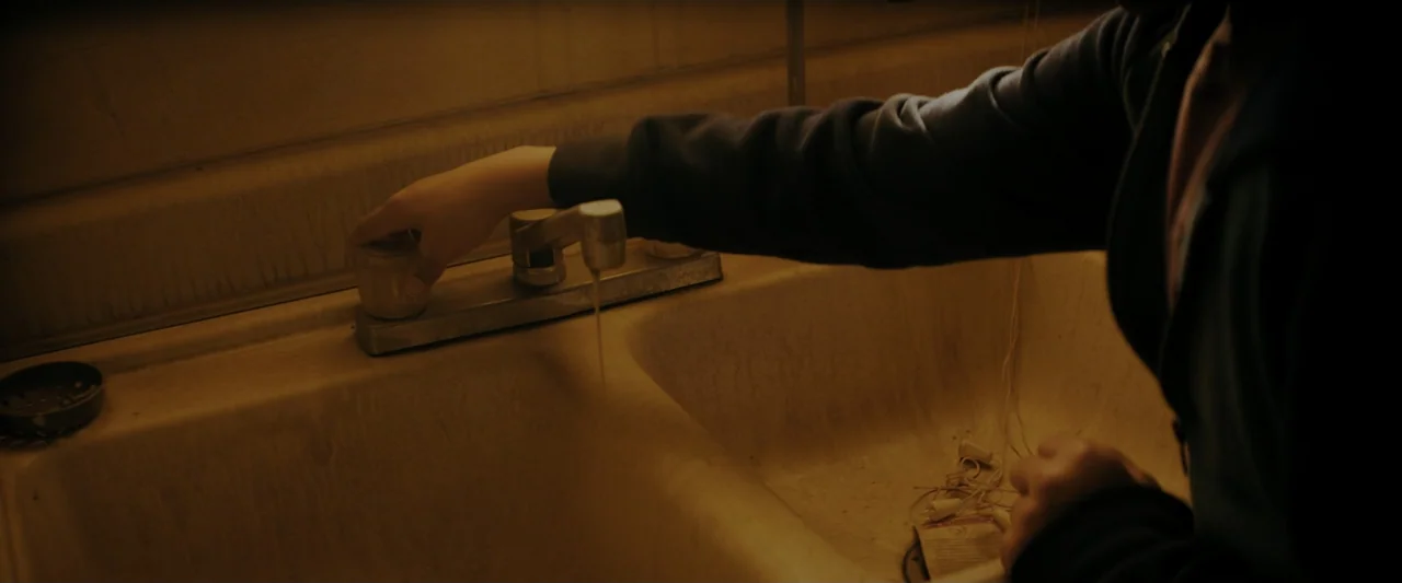 Encounter (2018) movie still: medium — A worn ceramic double-basin sink shows signs of age and staining. A person in a dark jacket reaches out to…
