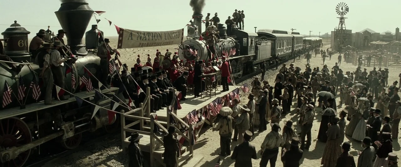 The Lone Ranger (2013) movie still: wide — A desert train station hosts a large crowd gathered for a historic rail ceremony. People stand around two…
