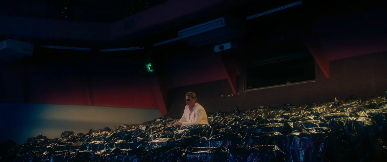 Pacifiction (2022) movie still: wide — The interior of a darkened movie auditorium features rows of chairs draped in plastic. A single man occupies…