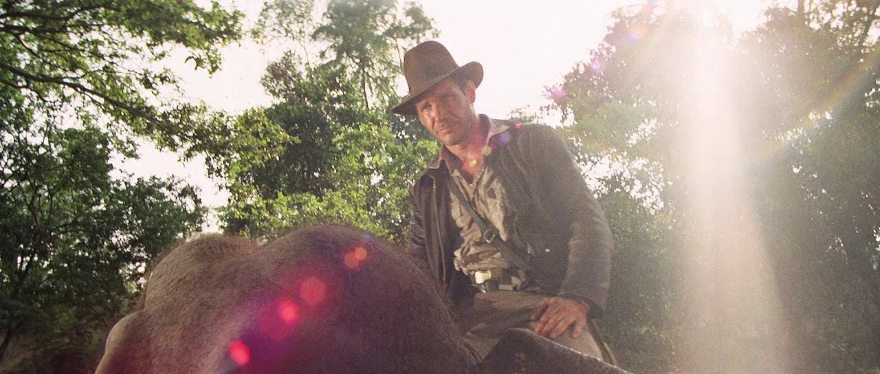 Indiana Jones and the Temple of Doom (1984) movie still: medium — A man sits on the back of an animal in a dense tropical environment. Sunlight…