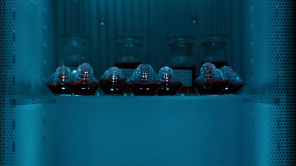 We Are The Night (2010) movie still: closeup — A dark, perforated metallic cabinet interior is bathed in an intense blue light. Several small glass…