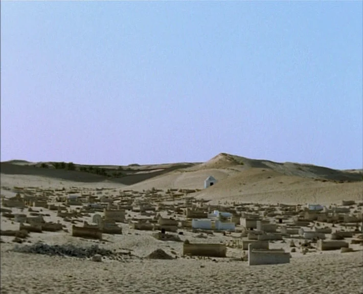 Fata Morgana (1971) movie still: establishing — A vast, sprawling cemetery occupies a barren desert landscape with sand dunes in the distance.…