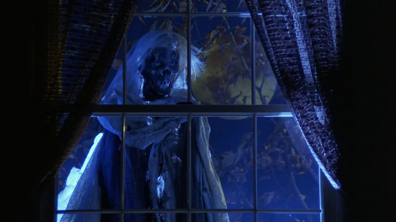 Creepshow (1982) movie still: medium — A ghoulish figure with pale tattered garments stands outside a paned window at night. A full yellow moon is…