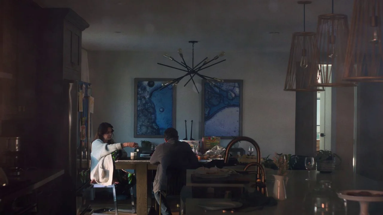 She Dies Tomorrow (2020) movie still: wide — A modern home dining area features a large table beneath a geometric sputnik chandelier. Two people sit…