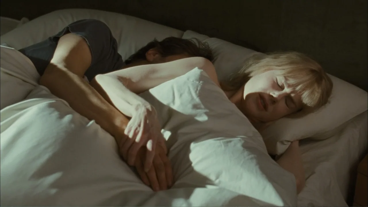 Before I Go to Sleep (2014) movie still: medium — A modern bedroom with white bedsheets and soft pillows during the daytime. A man and a woman lie…