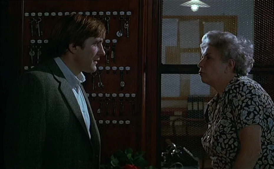 The Woman Next Door (1981) movie still: medium — A dimly lit hotel reception area features a wooden key board hanging on walls. A man in a blazer…
