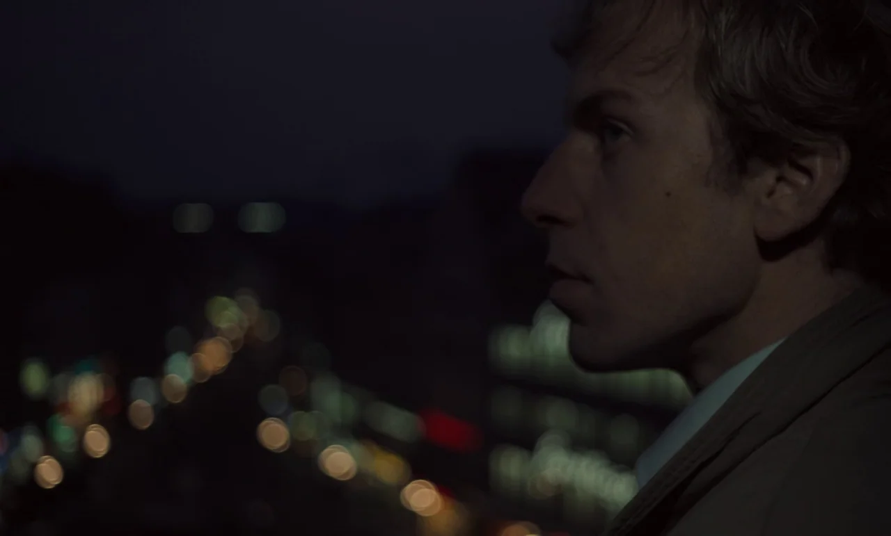 Wrong Move (1975) movie still: closeup — A man stands on an elevated vantage point overlooking a blurry urban nighttime landscape. He gazes into the…