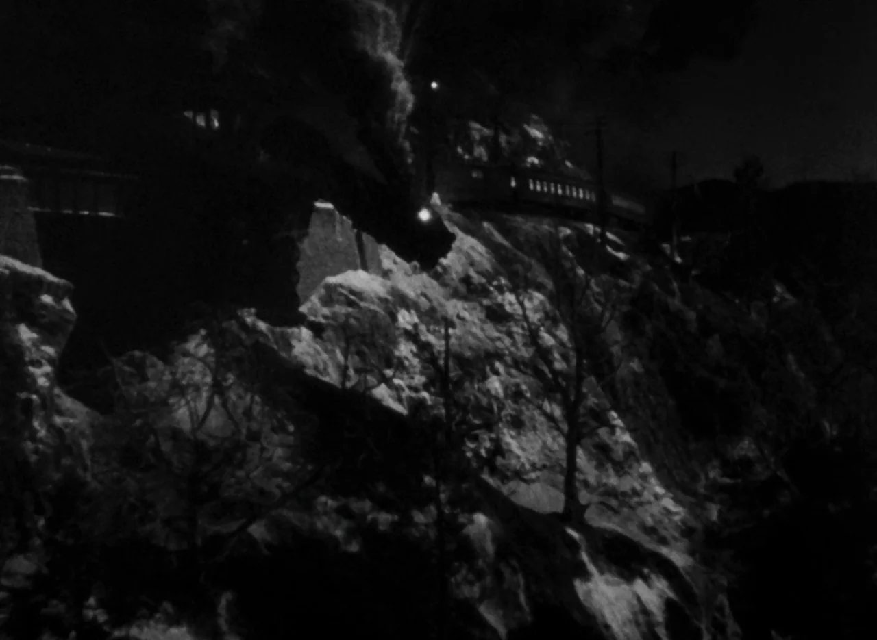 The Invisible Man (1933) (1933) movie still: wide — A steam locomotive passes along a dark, rugged mountain side at night. Steam billows from the…
