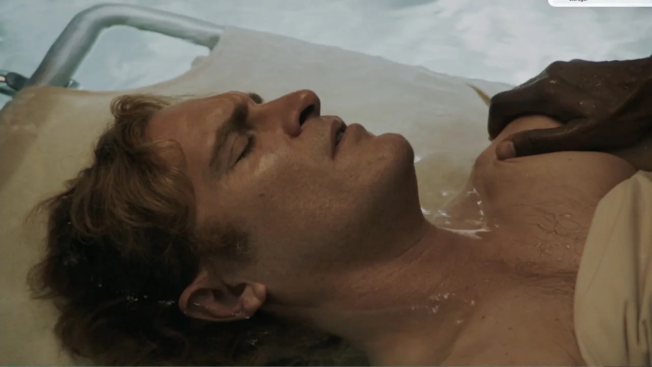 Don't Worry, He Won't Get Far on Foot (2018) movie still: closeup — A person floats in shallow water within a pool, partially submerged. Another…