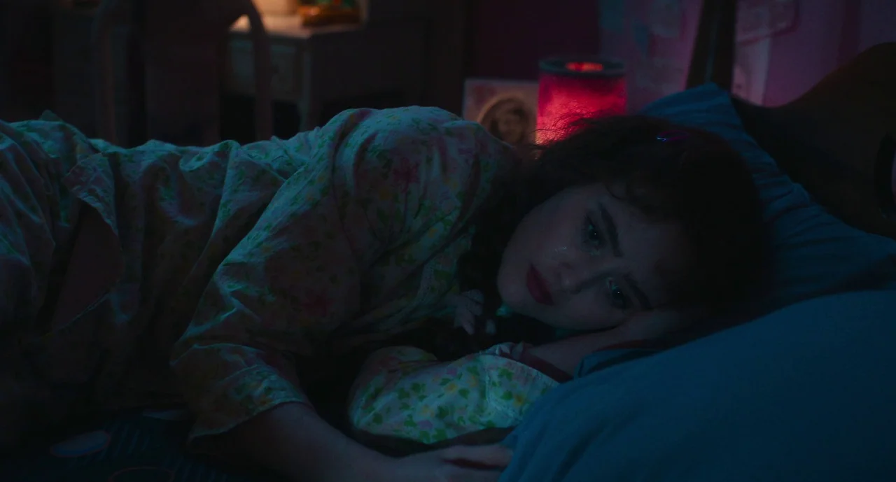 Lisa Frankenstein (2024) movie still: closeup — A dark bedroom illuminated by red and blue light sources creates deep color contrast. A young woman…
