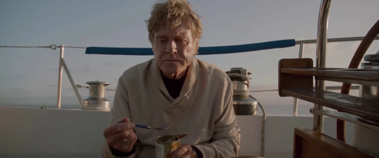 All Is Lost (2013) movie still: medium — A sailboat deck features polished steel rigging components under a clear evening sky. A man sits and eats…