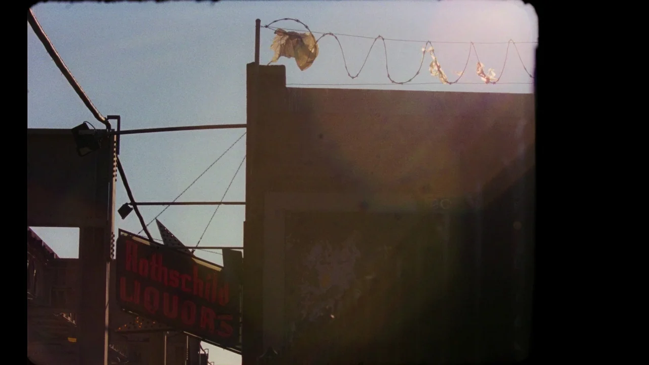 Pass Over (2018) movie still: wide — An exterior wall of a building features a liquor store sign and barbed wire. Plastic debris is snagged on the…