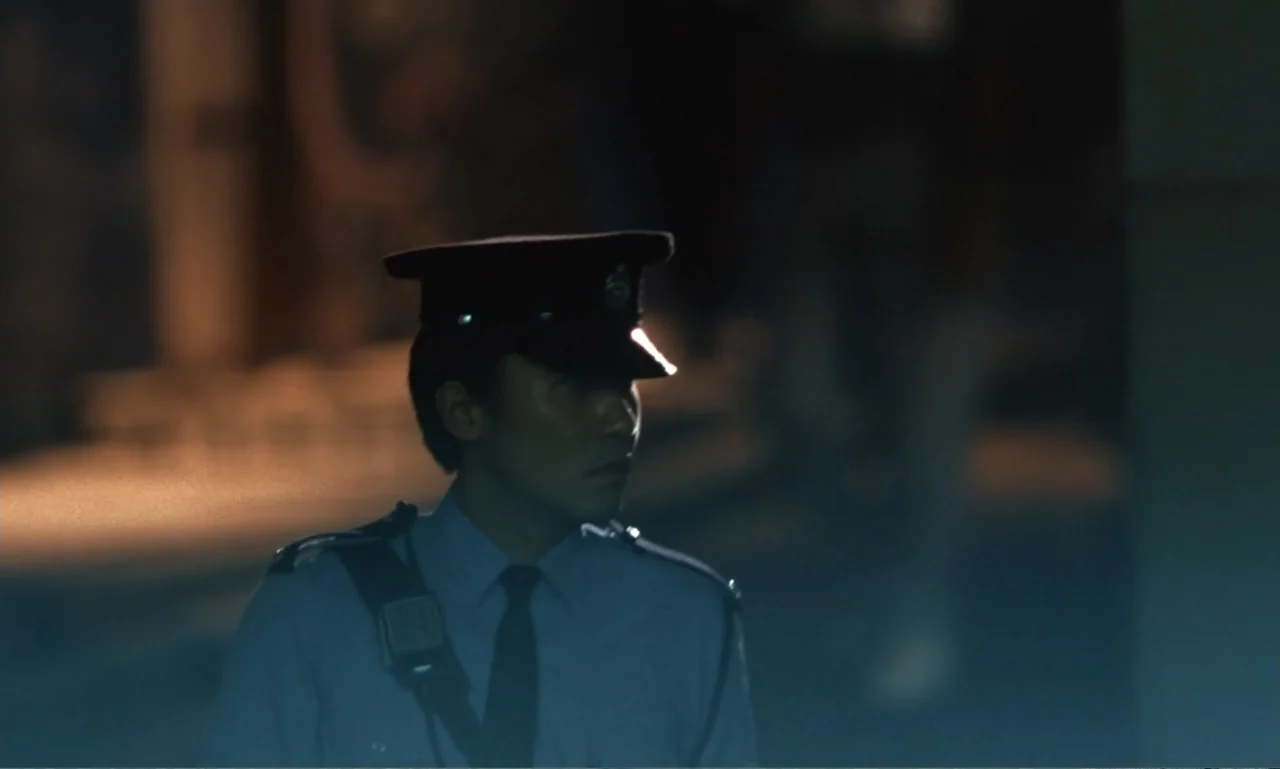 Chungking Express (1994) movie still: medium — A nighttime urban street at night with a security guard in uniform. The man stands against a darkened…