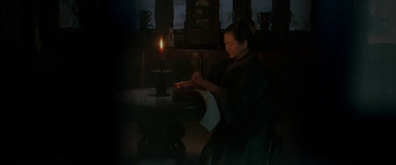 Crouching Tiger, Hidden Dragon (2000) movie still: medium — A dark, dimly lit room contains an ornate carved wooden table and chairs. A woman in…