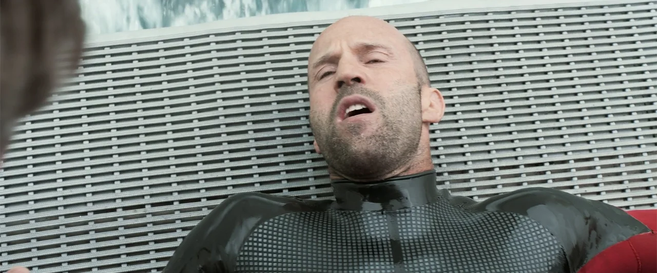The Meg (2018) movie still: closeup — A top-down view shows a textured metal grating surface on a boat deck. A man in a wetsuit lies flat on his…
