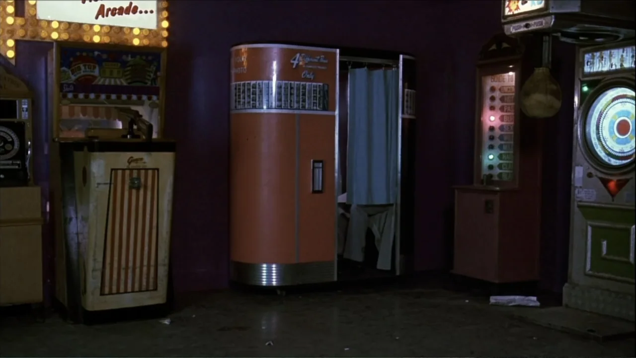 The Mambo Kings (1992) movie still: wide — An interior shot of an arcade featuring a vintage photo booth and various machines. The room is dimly lit…