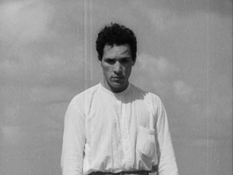 Redes (1936) movie still: medium — An open expanse under a bright, overcast sky forms the backdrop. A man in a plain white shirt stands still while…