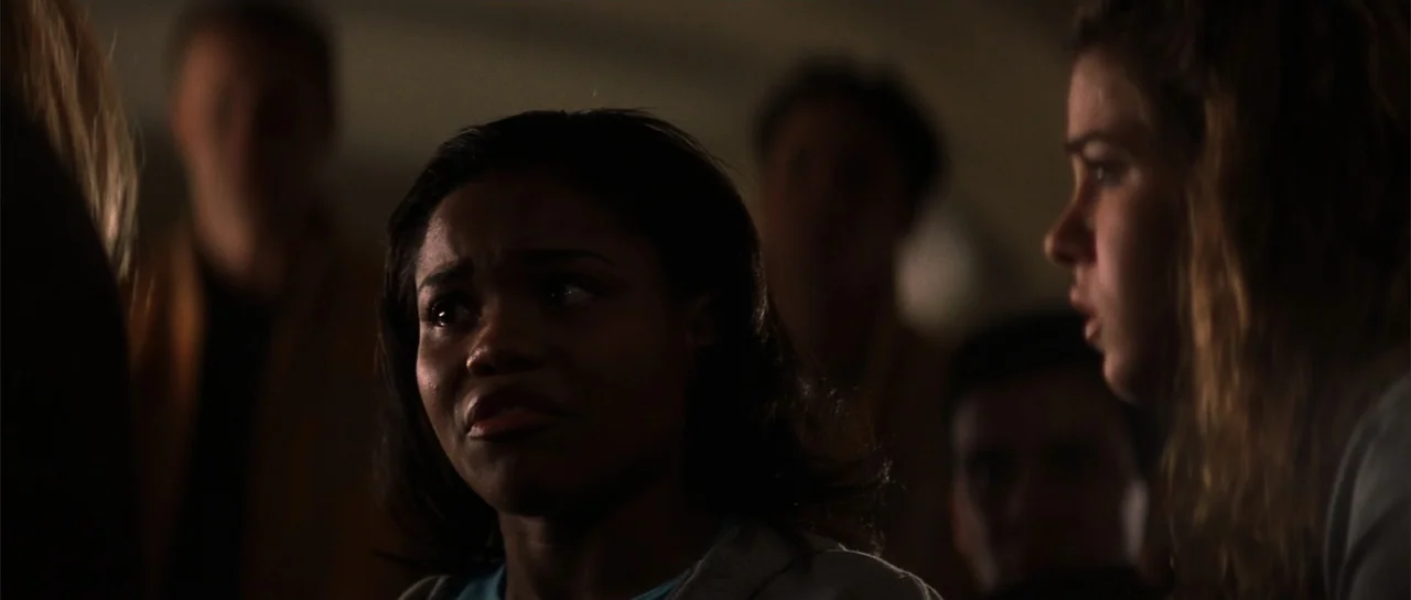 Jeepers Creepers 2 (2003) movie still: medium — A dark, out-of-focus indoor space contains a group of people sitting together. A young Black woman…