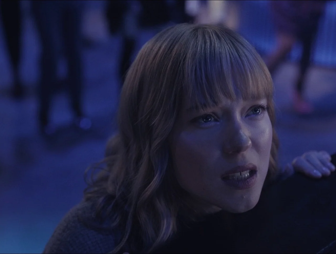 Transformers: Rise of the Beasts (2023) movie still: closeup — A dark, dimly lit nightclub interior with blurred figures moving in the background. A…