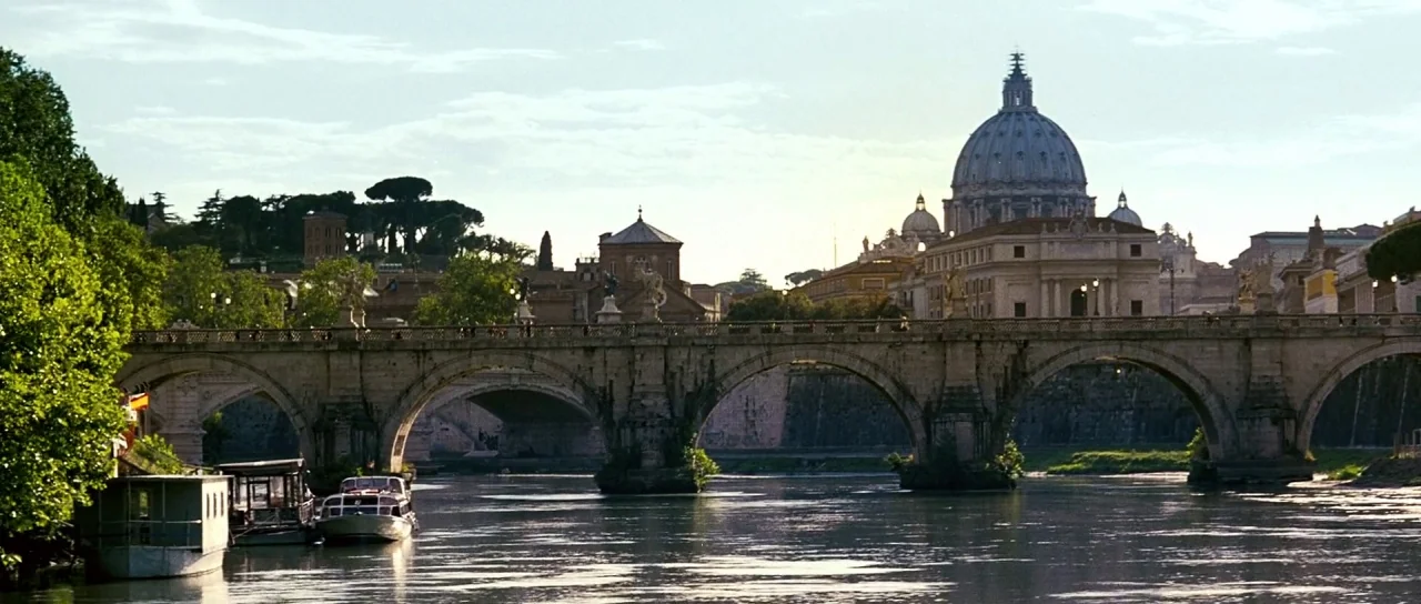 Down With Love (2003) movie still: establishing — An arched stone bridge spans the Tiber River with a large domed cathedral in distance. The stone…