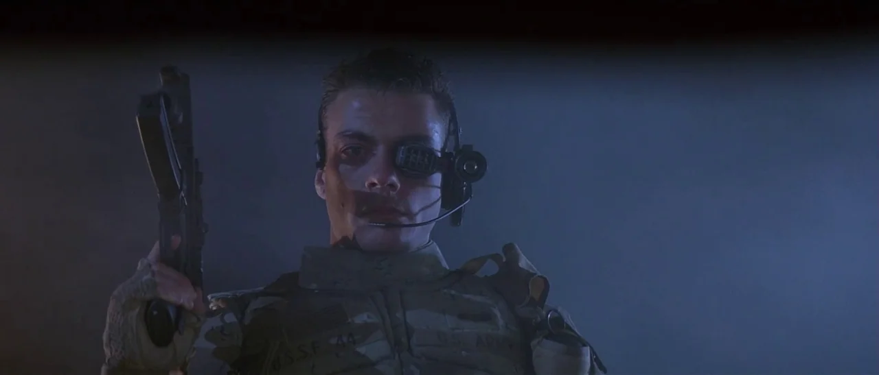 Universal Soldier (1992) movie still: medium — A dark, dimly lit environment with blue ambient light filling the frame space. A man wearing tactical…