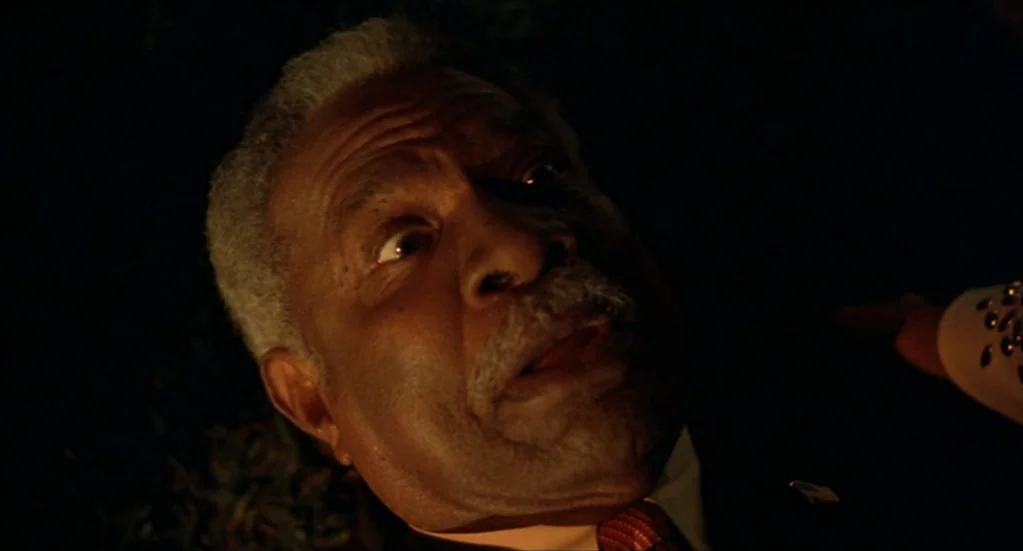Bubba Ho-Tep (2002) movie still: closeup — An elderly man is framed closely in a dark, shadow-filled environment at night. He stares intensely…