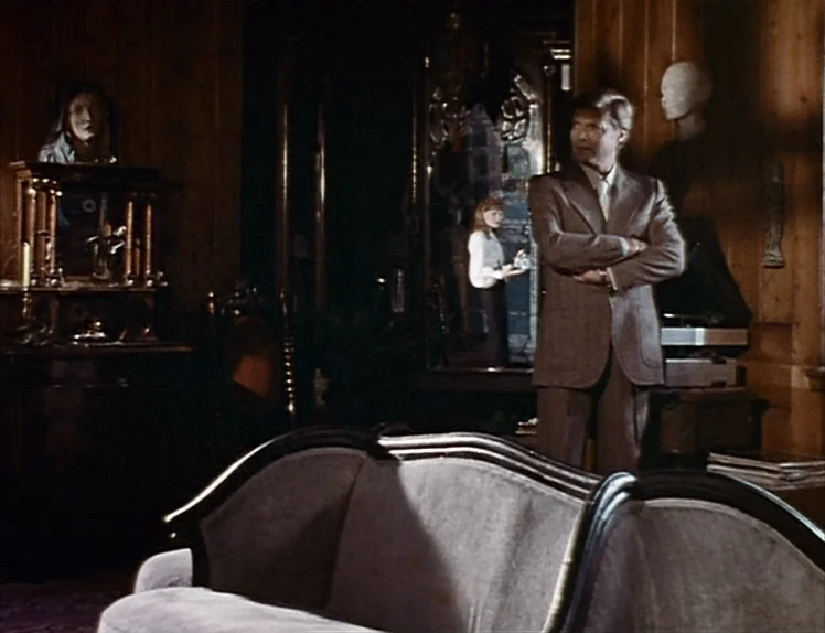 Martha (1974) movie still: medium — A dark, wood-paneled room is filled with ornate antique furniture and decorative sculptures. A man in a brown…