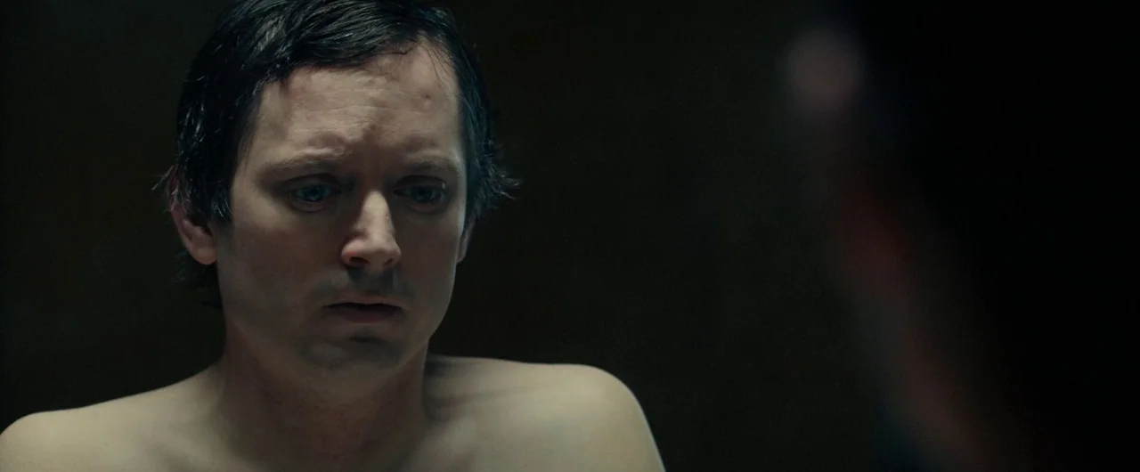 No Man of God (2021) movie still: closeup — A dark, dimly lit room serves as the setting for this interaction. A bare-chested man looks down,…