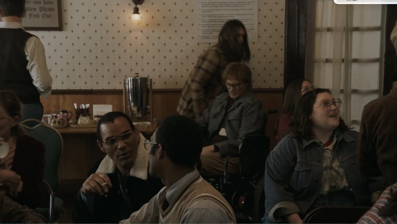 Don't Worry, He Won't Get Far on Foot (2018) movie still: medium — A room with wallpapered walls displays meeting information on paper posters for…
