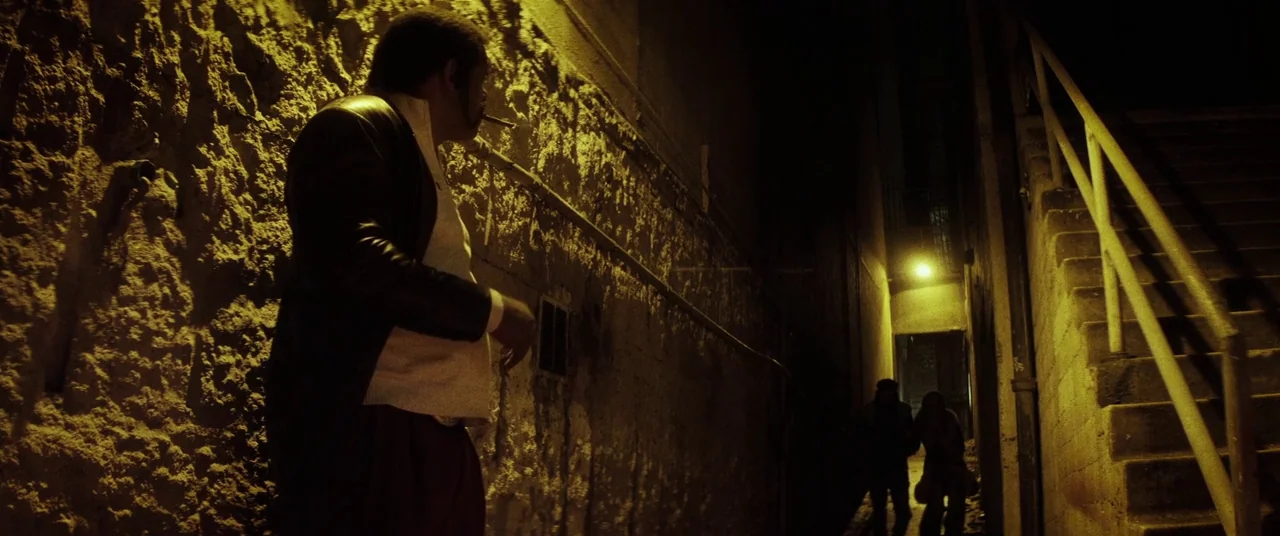Lords Of Salem (2013) movie still: medium — A narrow stone alley at night with a metal staircase on the right. A man stands in the foreground…