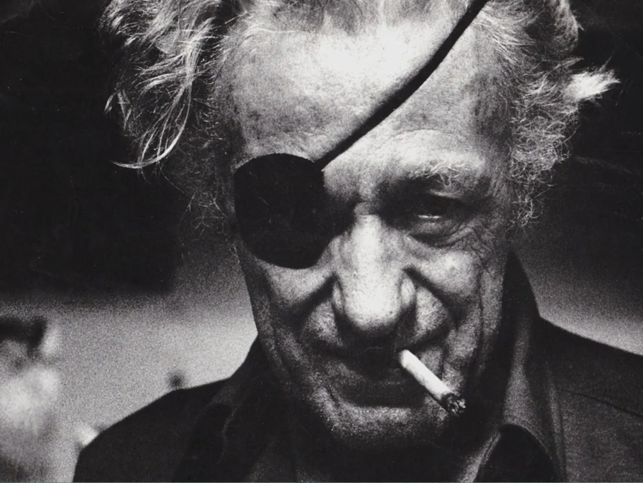 Don't Expect Too Much (2011) movie still: closeup — A dark indoor space provides the setting for this portrait. An older man wearing an eye patch…