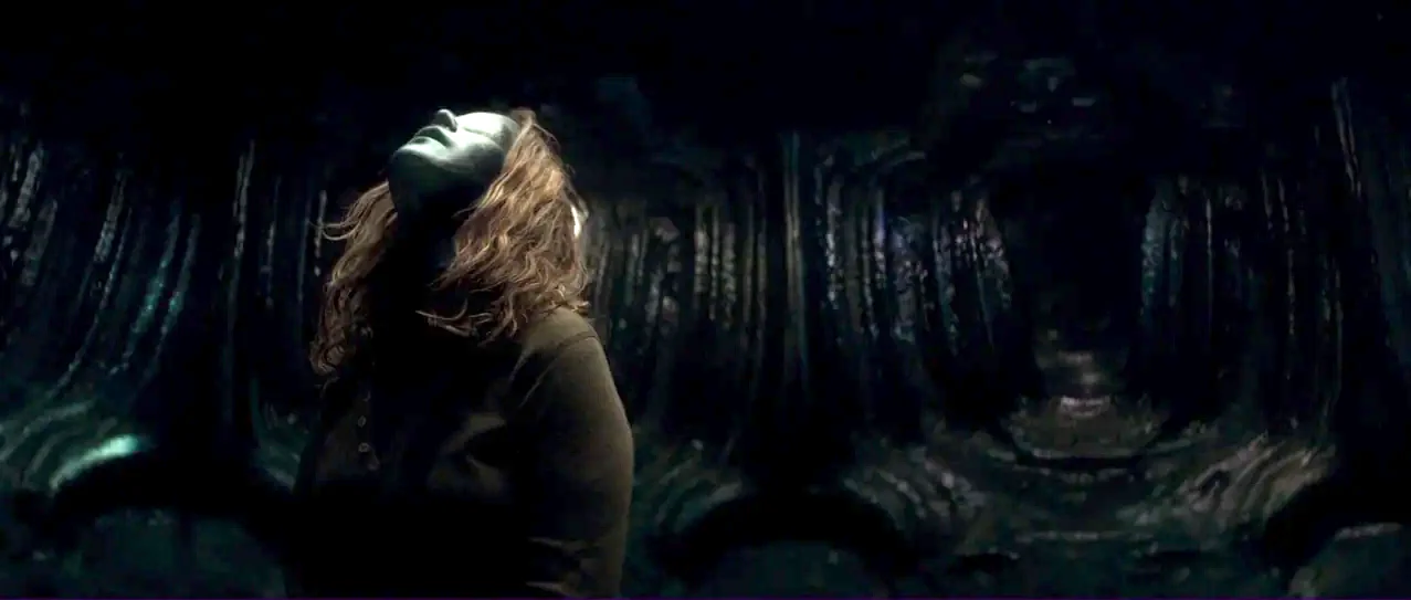 Annihilation (2018) movie still: medium — A dark, cavernous space is lined with organic, ribbed wall textures. A woman looks upward toward the top…