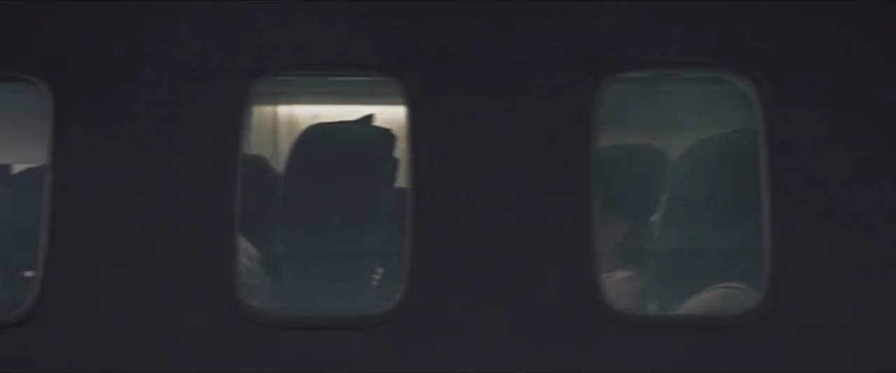 Darkest Hour (2017) movie still: medium — A dark airplane cabin interior viewed through a row of small, reflective passenger windows. The silhouette…