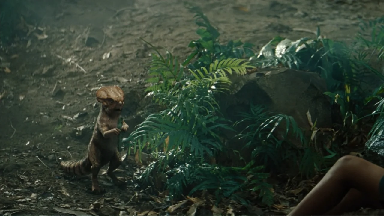 Jurassic World Rebirth (2025) movie still: medium — A dense, shaded floor of a humid jungle covered in dead leaves and ferns. A small, bipedal…