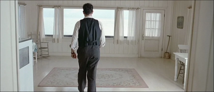 Road To Perdition (2002) movie still: fullbody — A bright cottage room features white wood-paneled walls and a window overlooking the ocean. A man…