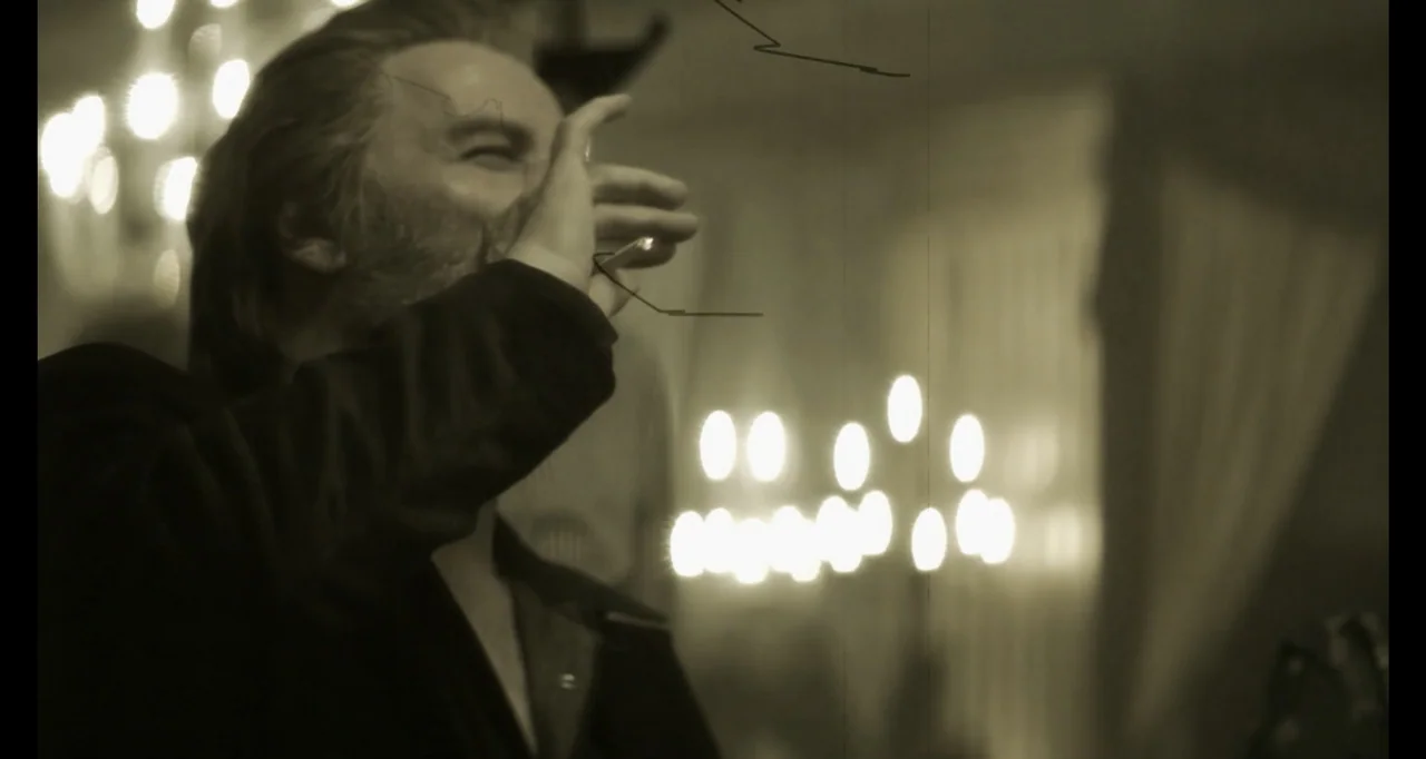 The Poison Rose (2019) movie still: medium — A dimly lit room contains a man holding a drinking glass near his mouth. The background features bright…