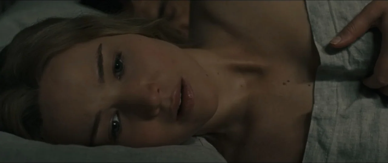 mother! (2017) movie still: closeup — A dark bedroom features a person lying under grey linen sheets at night. The woman rests her head on a pillow…