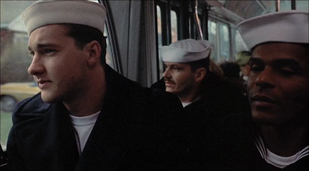 The Last Detail (1973) movie still: medium — Inside a bus with windows looking out onto a street, several sailors sit together. The sailors are…