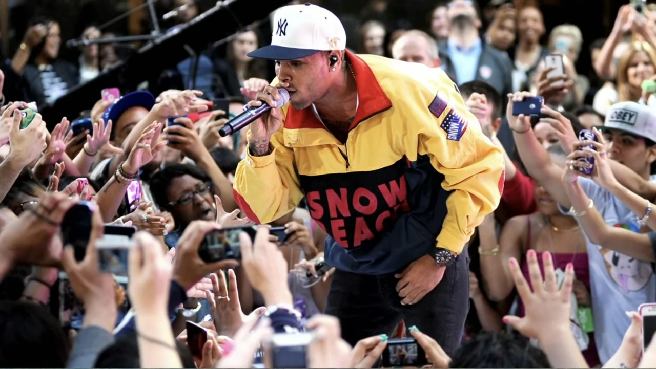 Chris Brown: A History of Violence (2024) movie still: medium — A dense crowd of fans surrounds a performer at an outdoor event. A man in a…