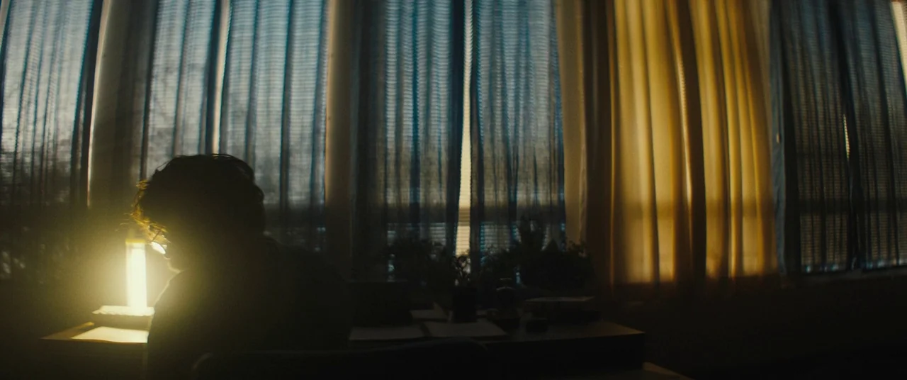 I Think We’re Alone Now (2018) movie still: medium — A workspace with floor-to-ceiling windows covered by translucent curtains letting in soft…