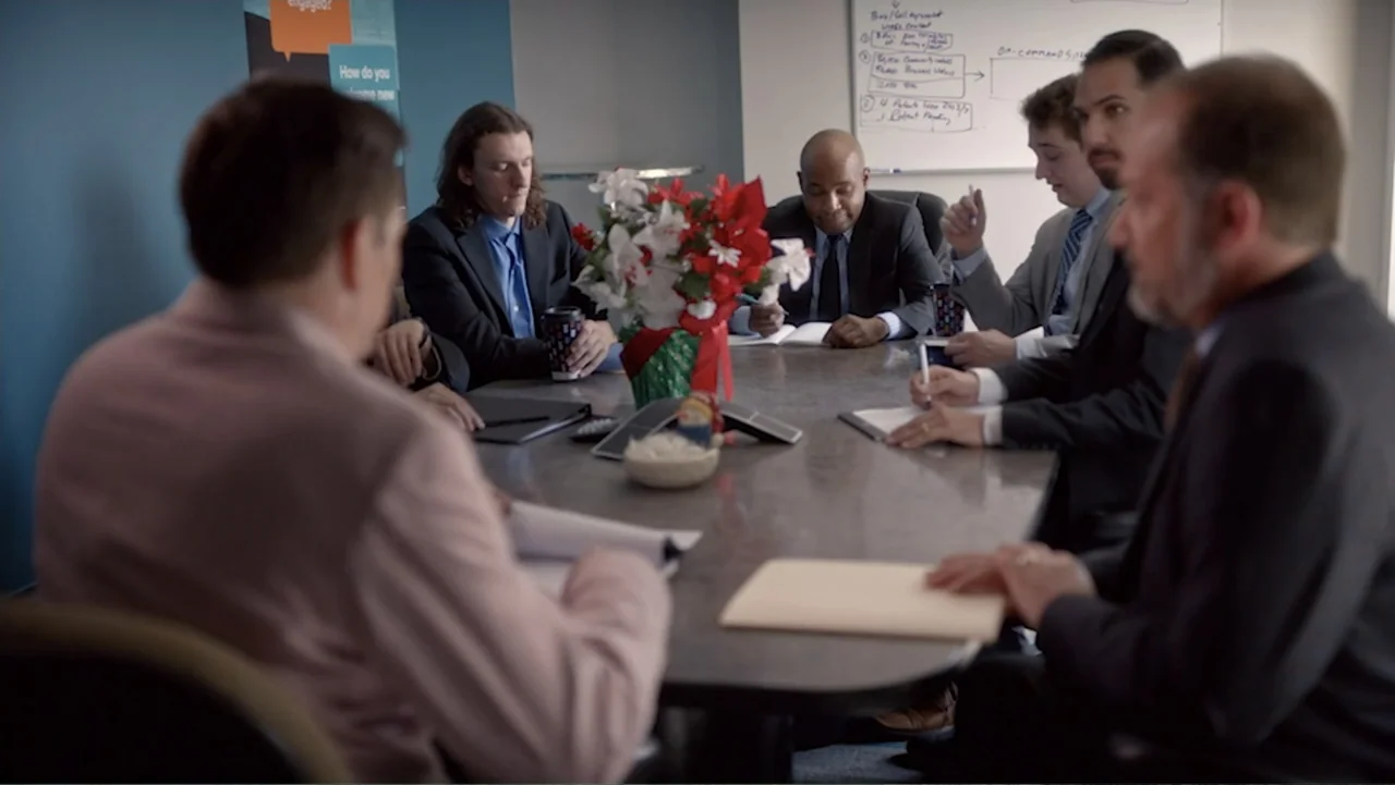 Ask Me to Dance (2022) movie still: medium — A modern business meeting space contains a dark wood table and a whiteboard. Several professional men…