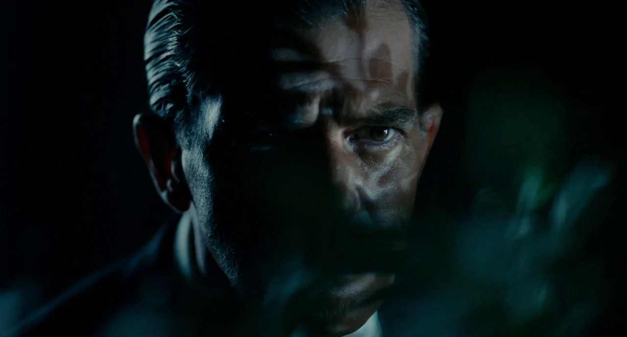 The Skin I Live In (2011) movie still: closeup — A dark, minimally lit space surrounds the close-up view of a man's face. Sharp shadows partially…