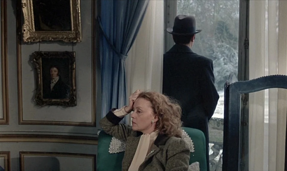 Mr. Klein (1976) movie still: medium — An elegant, traditional room with blue walls, framed portraits, and white curtains. A woman sits in a green…