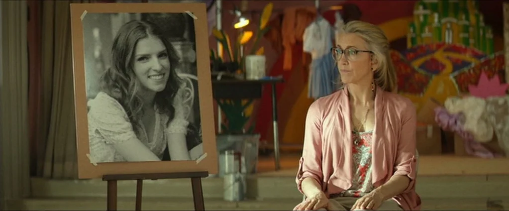 Cake (2014) movie still: medium — A woman sits in a workspace filled with art supplies and a painted backdrop. Beside her, an easel displays a large…