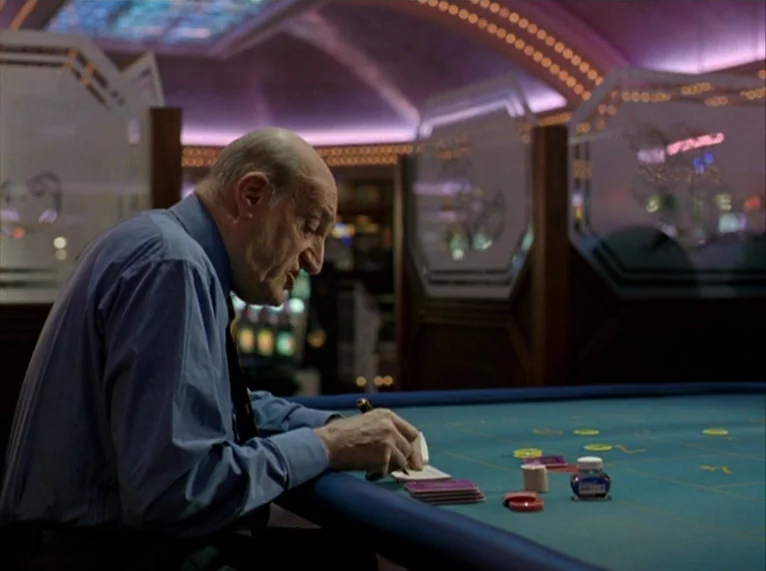 For Ever Mozart (1996) movie still: medium — A dimly lit room with high ceilings and decorative glass partitions on the gaming floor. An elderly man…