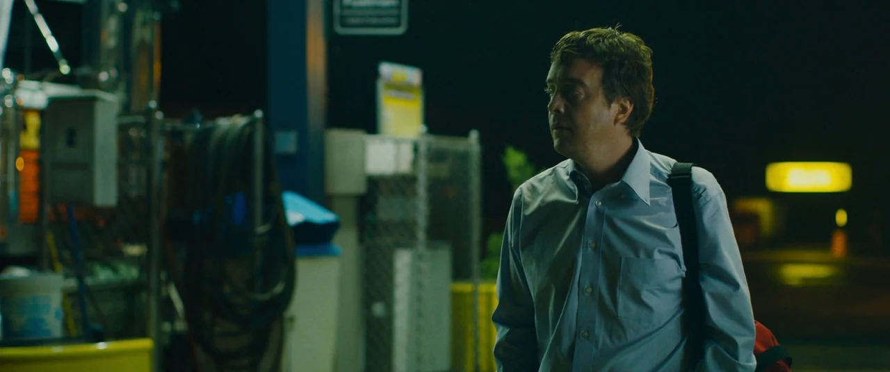 Blue Ruin (2013) movie still: medium — A night exterior at a gas station with metallic structures and industrial storage racks. A man wearing a…